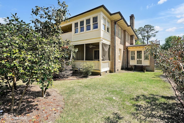 back of property featuring a sunroom, a lawn, entry steps, brick siding, and a chimney
