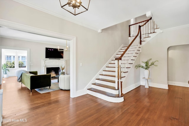 staircase with ornamental molding, baseboards, wood finished floors, and a fireplace