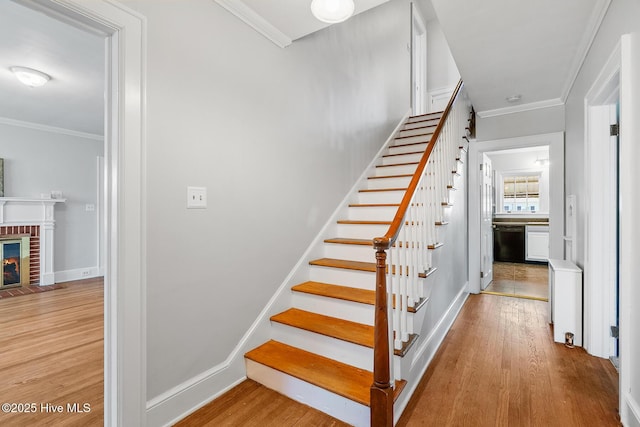 stairs with crown molding, a brick fireplace, wood finished floors, and baseboards