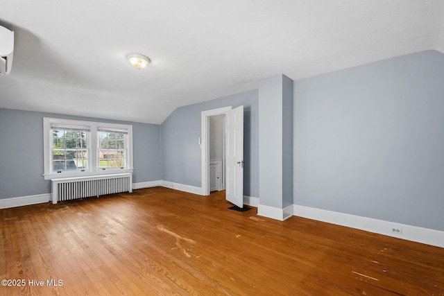 bonus room featuring baseboards, vaulted ceiling, a wall mounted air conditioner, radiator heating unit, and wood finished floors
