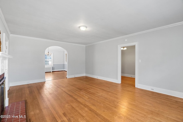 unfurnished living room with arched walkways, crown molding, and light wood-type flooring