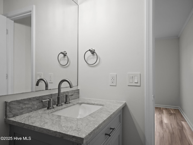 bathroom with crown molding, wood finished floors, vanity, and baseboards
