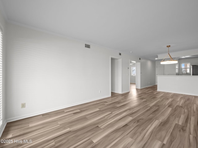 unfurnished living room with light wood-style flooring, ornamental molding, baseboards, and a sink