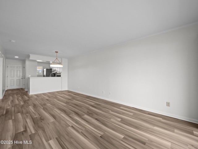 unfurnished living room with wood finished floors, baseboards, and ornamental molding