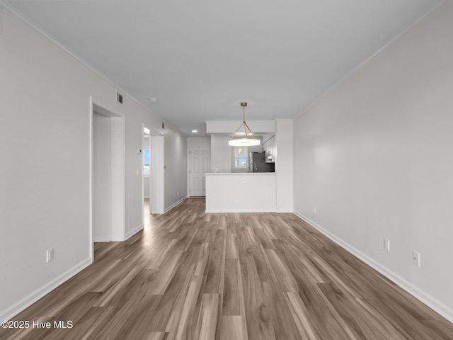 unfurnished living room with wood finished floors, crown molding, and baseboards