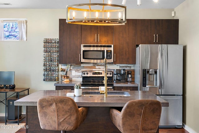kitchen featuring dark brown cabinets, wood finished floors, baseboards, appliances with stainless steel finishes, and visible vents