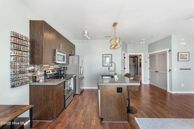 kitchen featuring a breakfast bar area, a sink, stainless steel appliances, dark wood-type flooring, and an island with sink