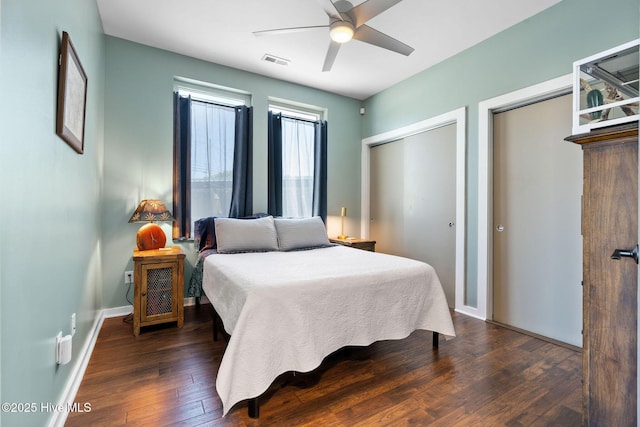 bedroom featuring hardwood / wood-style flooring, baseboards, visible vents, a ceiling fan, and multiple closets
