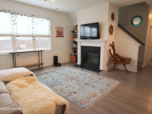 living area featuring a fireplace with flush hearth, wood finished floors, a ceiling fan, baseboards, and stairs