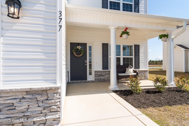 view of exterior entry with stone siding and covered porch