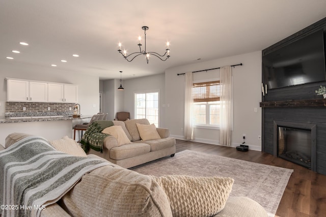 living room with a fireplace, baseboards, a notable chandelier, dark wood-style floors, and recessed lighting