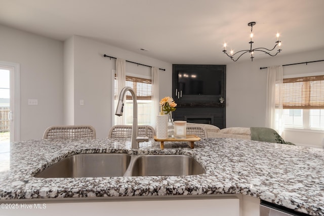 kitchen featuring light stone countertops, stainless steel dishwasher, a sink, and a notable chandelier