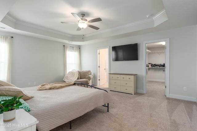 bedroom with a walk in closet, light colored carpet, a raised ceiling, and crown molding