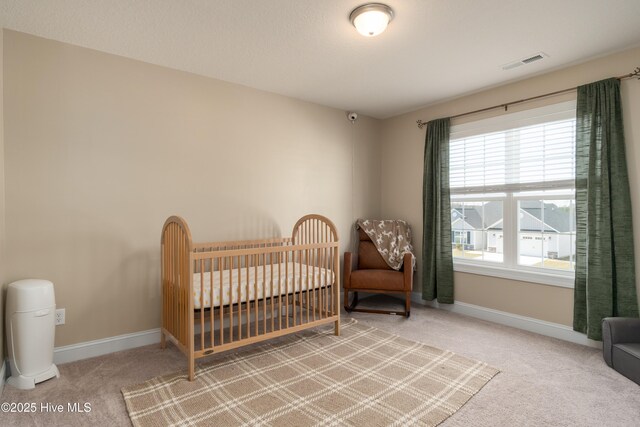 bedroom with baseboards, carpet flooring, a crib, and visible vents