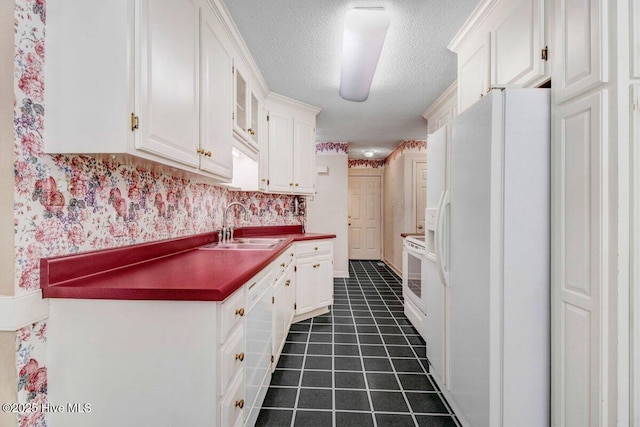 kitchen featuring white appliances, a sink, a textured ceiling, white cabinetry, and dark tile patterned flooring