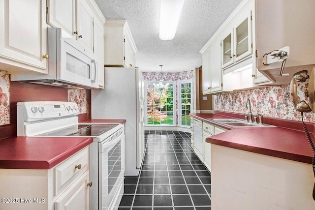 kitchen featuring white appliances, a sink, a textured ceiling, wallpapered walls, and dark countertops
