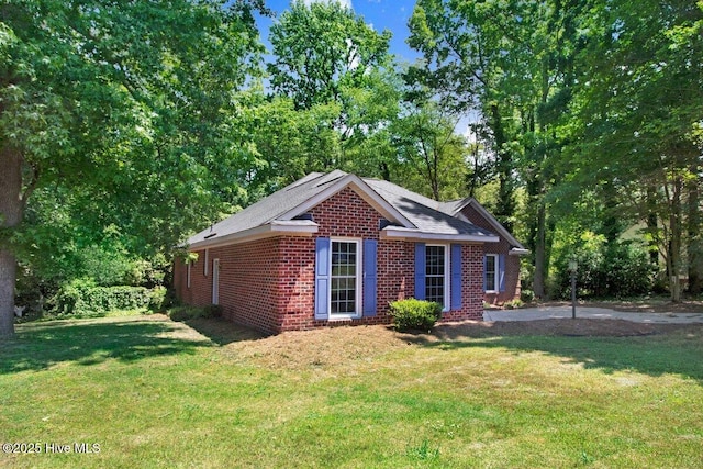 view of side of property featuring brick siding, a yard, and view of wooded area
