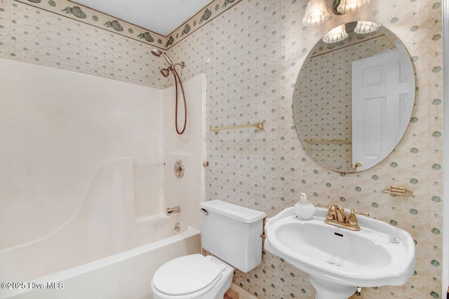 bathroom with a sink, toilet,  shower combination, wallpapered walls, and a chandelier