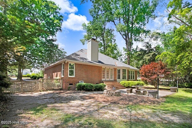rear view of property with brick siding, french doors, a chimney, fence, and a patio