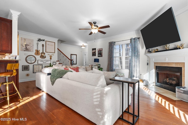 living area featuring a fireplace, stairway, a ceiling fan, crown molding, and wood finished floors