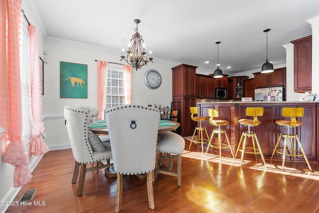 dining space featuring light wood-type flooring, a notable chandelier, ornamental molding, and visible vents