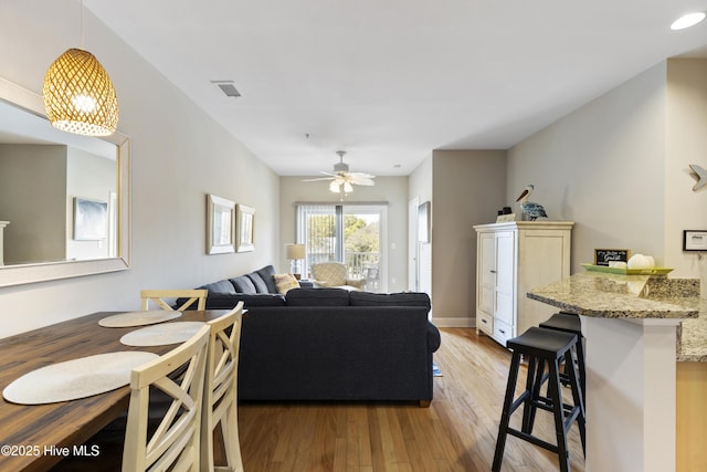 living room featuring baseboards, a ceiling fan, light wood finished floors, and visible vents