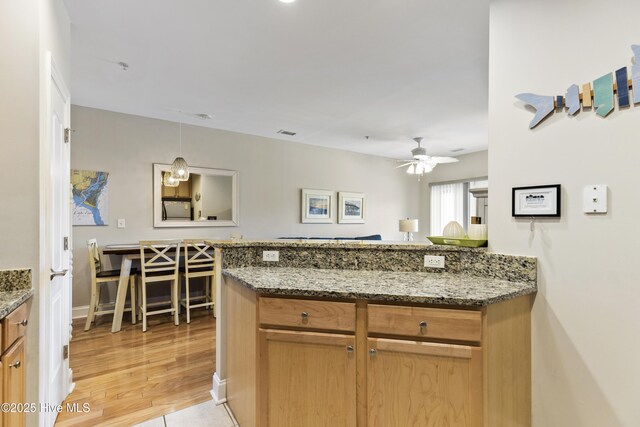 kitchen with a peninsula, light wood-type flooring, stone counters, a ceiling fan, and pendant lighting