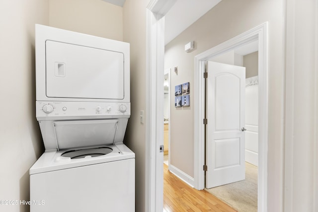 laundry area with stacked washer / drying machine, light wood-style flooring, baseboards, and laundry area