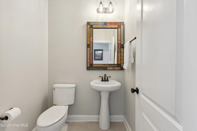 half bath with toilet, baseboards, tile patterned floors, and a sink