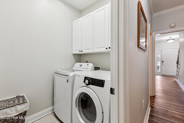 clothes washing area with cabinet space, washing machine and clothes dryer, baseboards, ornamental molding, and light wood finished floors