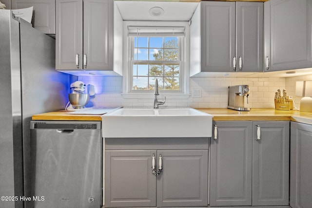 kitchen with light countertops, gray cabinets, decorative backsplash, a sink, and dishwasher
