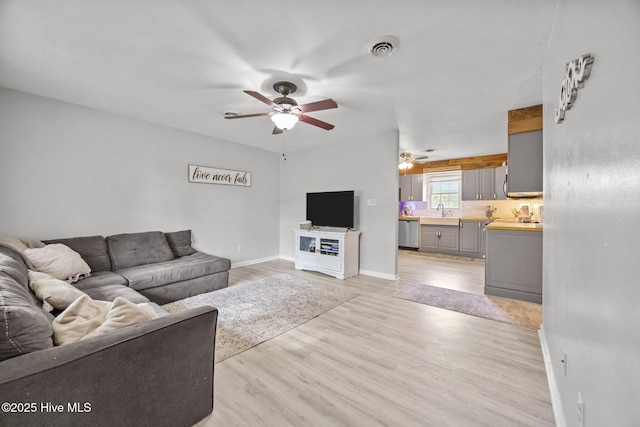 living room featuring baseboards, visible vents, light wood-style floors, and a ceiling fan