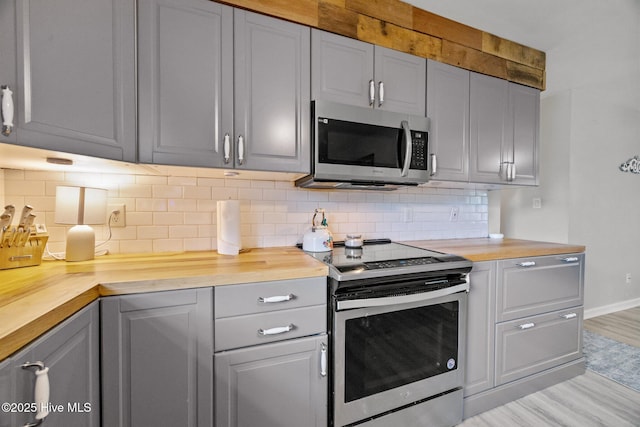 kitchen featuring butcher block countertops, light wood-style flooring, appliances with stainless steel finishes, gray cabinetry, and backsplash