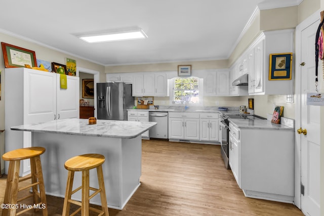 kitchen featuring ornamental molding, appliances with stainless steel finishes, under cabinet range hood, white cabinetry, and a breakfast bar area