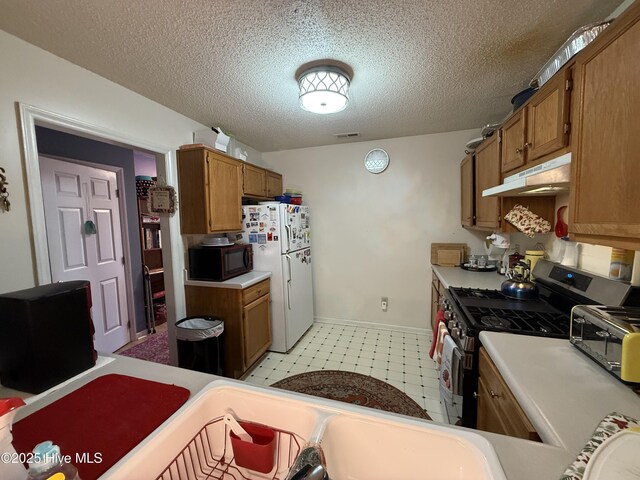 kitchen with black microwave, stainless steel range with gas cooktop, freestanding refrigerator, under cabinet range hood, and visible vents