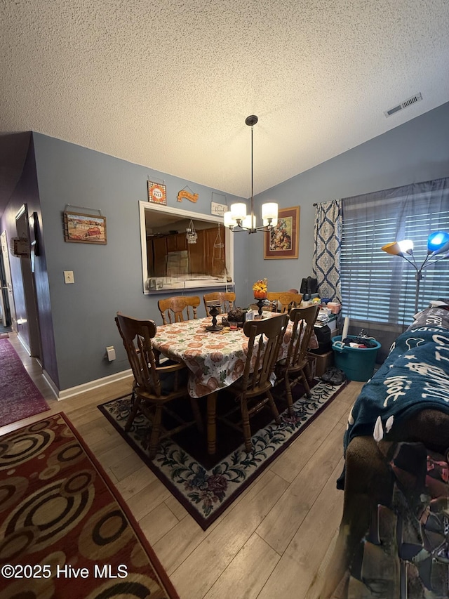 dining area featuring a textured ceiling, a notable chandelier, visible vents, and light wood-style floors