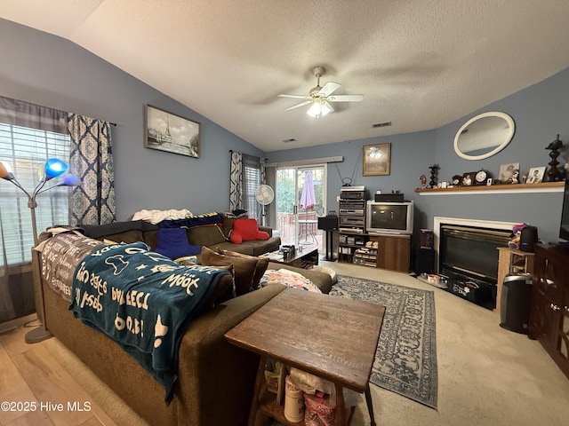 carpeted living room featuring a textured ceiling, ceiling fan, vaulted ceiling, and visible vents