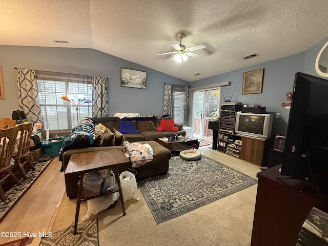 living area featuring a ceiling fan, a textured ceiling, visible vents, and lofted ceiling
