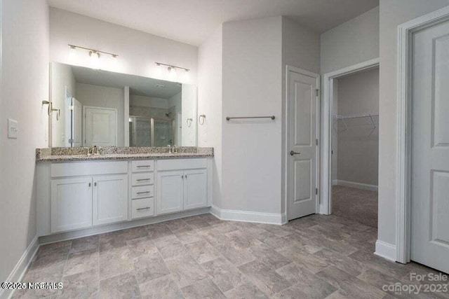 bathroom with double vanity, a walk in closet, a shower stall, a sink, and baseboards