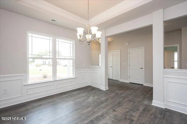 unfurnished dining area featuring a healthy amount of sunlight, a notable chandelier, dark wood-type flooring, and visible vents