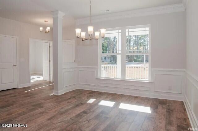 unfurnished dining area with ornamental molding, a decorative wall, dark wood-style floors, and a notable chandelier
