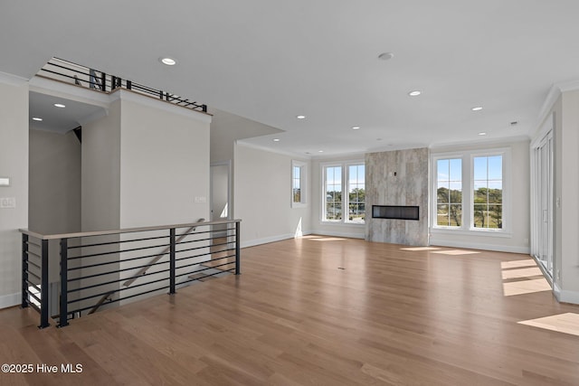 unfurnished living room with recessed lighting, wood finished floors, crown molding, and baseboards