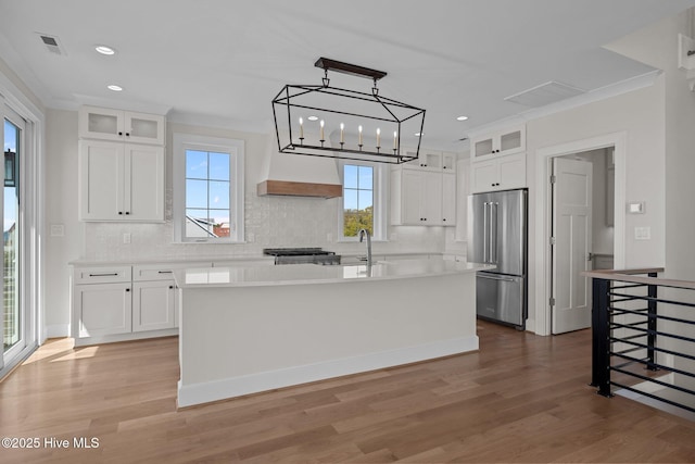 kitchen featuring tasteful backsplash, high end fridge, light wood finished floors, a center island with sink, and visible vents