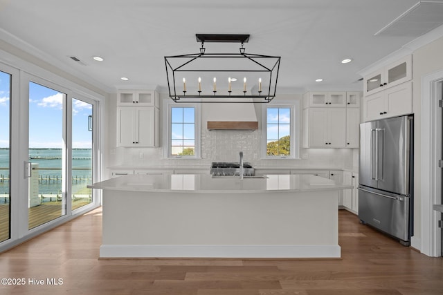 kitchen with light countertops, backsplash, an island with sink, and high end refrigerator