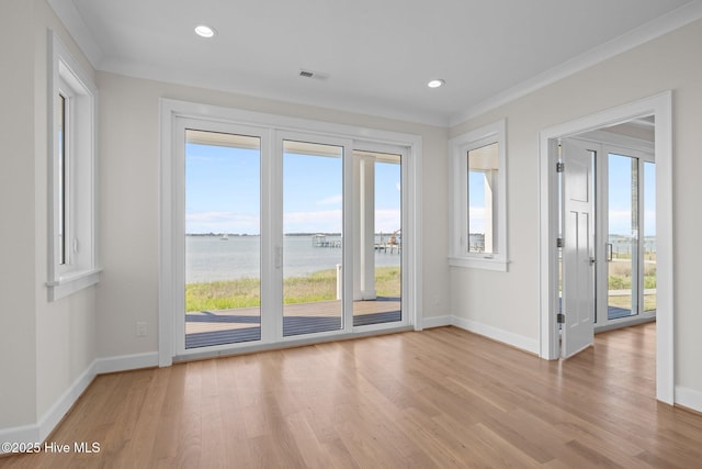 interior space featuring light wood finished floors, baseboards, a water view, and ornamental molding