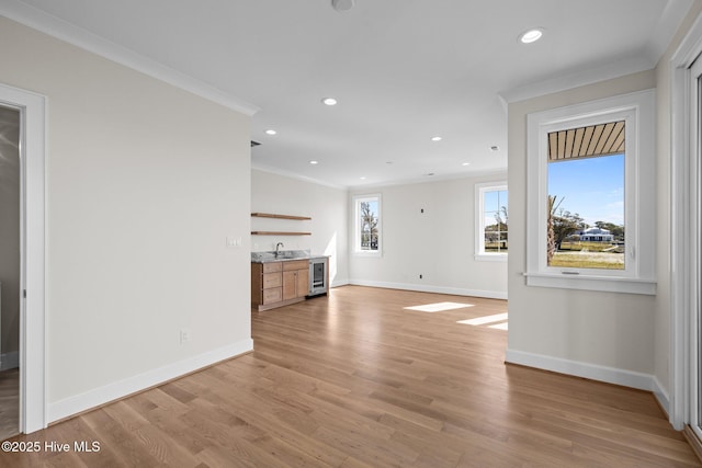 unfurnished living room featuring wine cooler, baseboards, ornamental molding, and wet bar