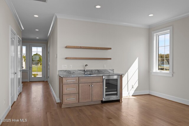 bar featuring dark wood finished floors, wet bar, baseboards, crown molding, and beverage cooler