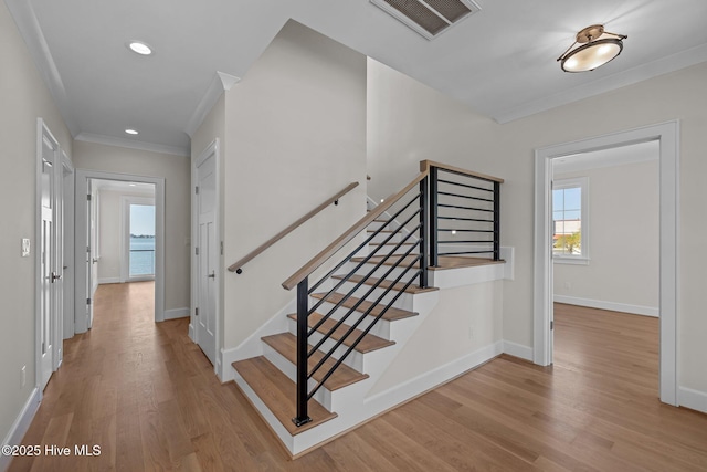 stairs with wood finished floors, visible vents, baseboards, and ornamental molding