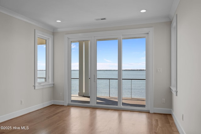 unfurnished room featuring a water view, visible vents, baseboards, wood finished floors, and ornamental molding