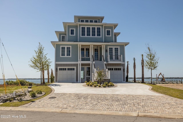 raised beach house with stairs, a water view, decorative driveway, a porch, and a garage